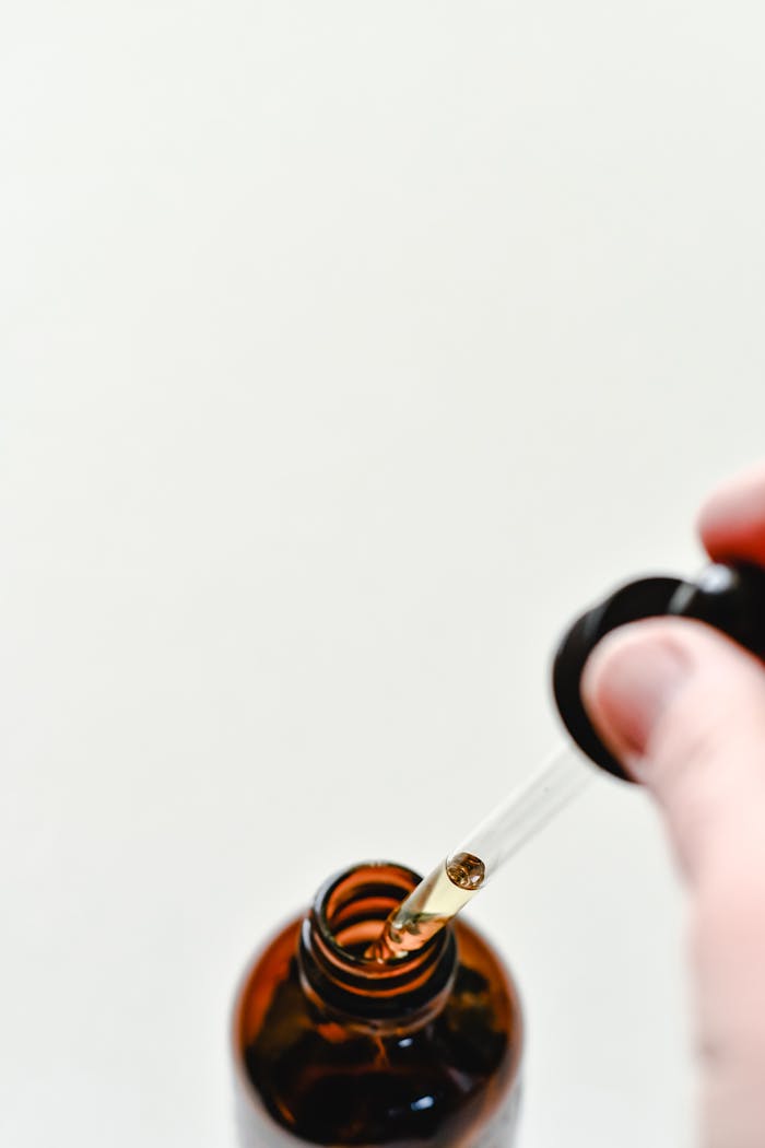 Close-up of a glass dropper with liquid above an amber bottle on a light background.
